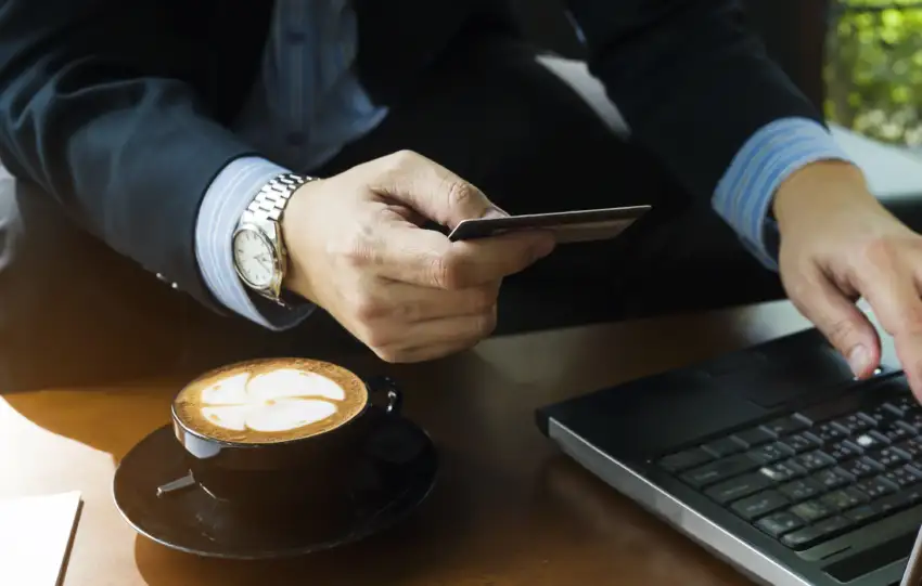 Čovek koristi laptop i drži platnu karticu dok kupuje male luksuze online