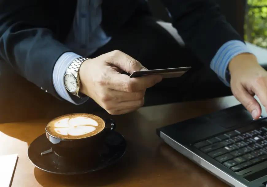 Čovek koristi laptop i drži platnu karticu dok kupuje male luksuze online