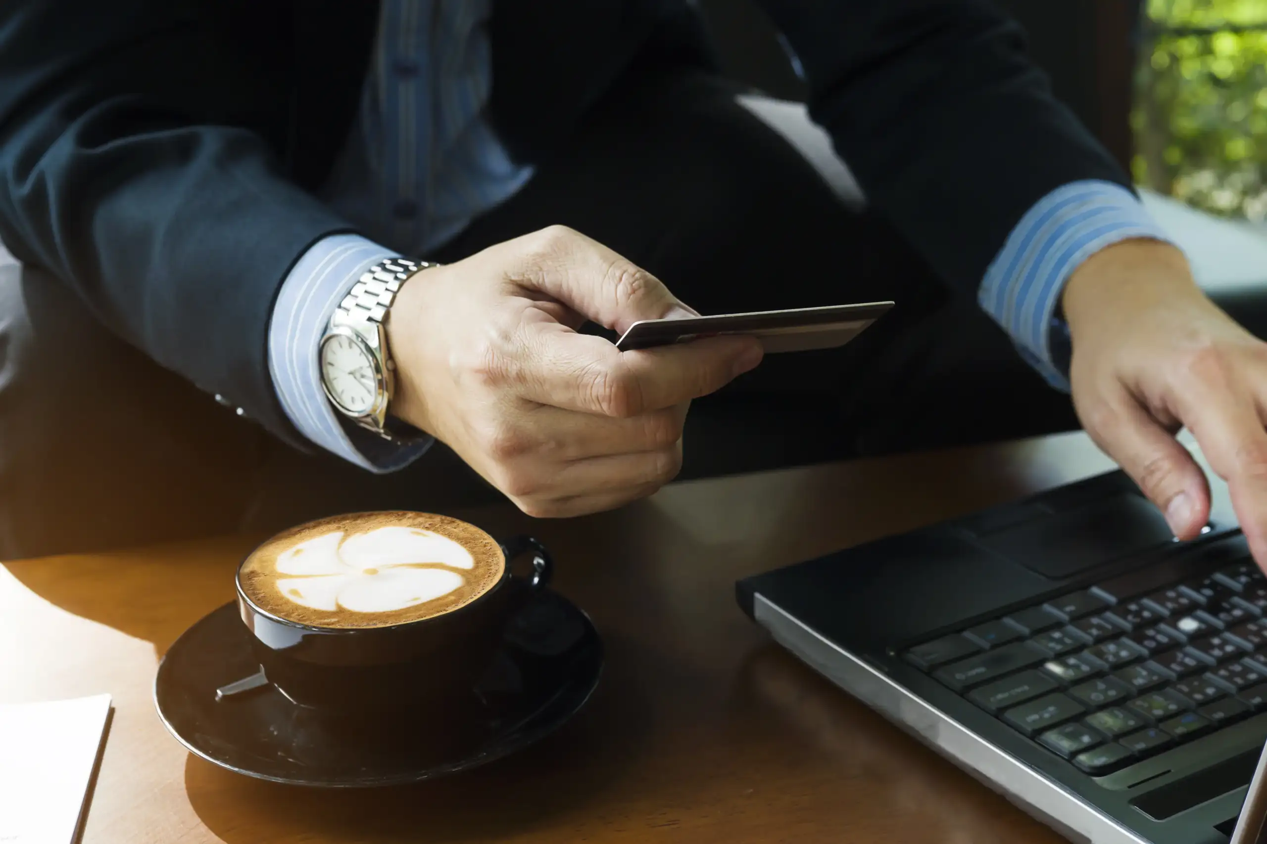 Čovek koristi laptop i drži platnu karticu dok kupuje male luksuze online